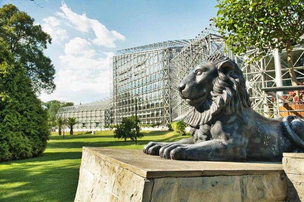 Der steinerne Löwe wacht über das Palmenhaus im Chopin-Park, wo tausende exotische Pflanzen unter dem markanten Glas-Stahl-Dach gedeihen.