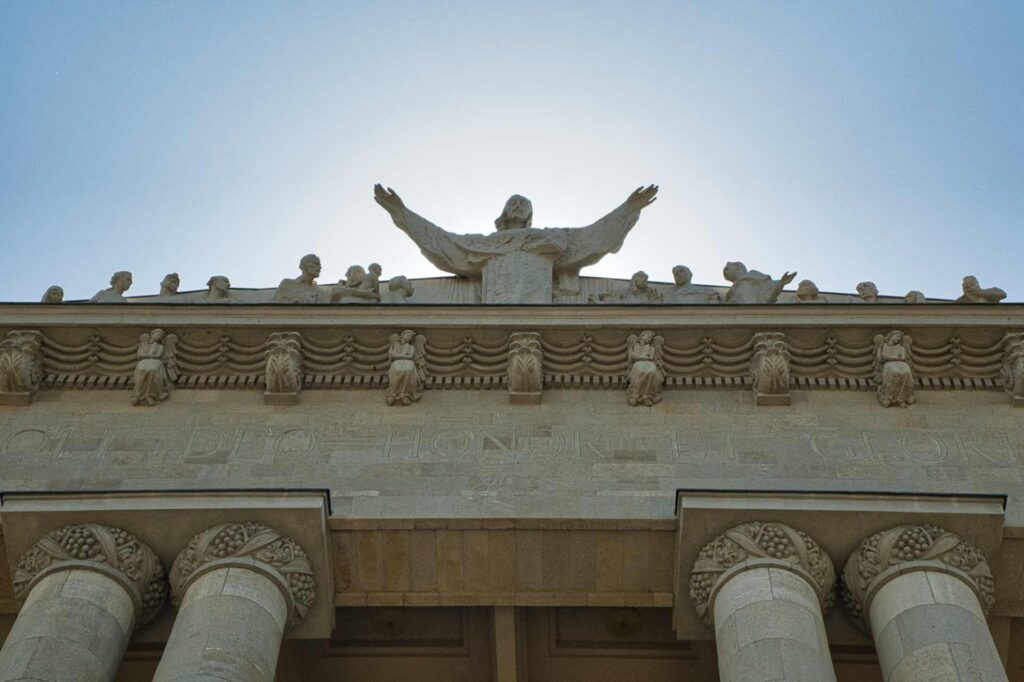 Die monumentale Figurengruppe über dem Portikus der Christkönigskathedrale (Archikatedra Chrystusa Króla) zeigt Christus mit ausgebreiteten Armen, umgeben von Apostelfiguren – darunter die lateinische Inschrift "Soli Deo Honor et Gloria" ("Gott allein Ehre und Ruhm").