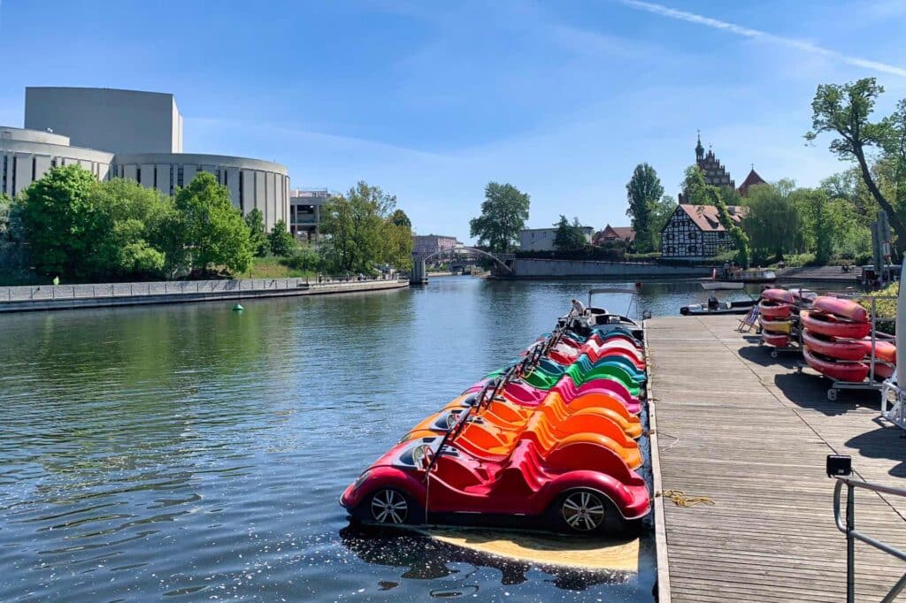 Colorful car-shaped pedal boats on the Brda River in Bydgoszcz, in front of the Opera Nova building
