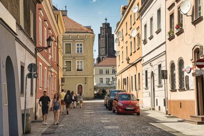 Ein Spaziergang durch die schmalen, farbenfrohen Altstadtgassen von Gliwice: Im Hintergrund ragt der Turm der Allerheiligenkirche &uuml;ber die D&auml;cher hinaus.